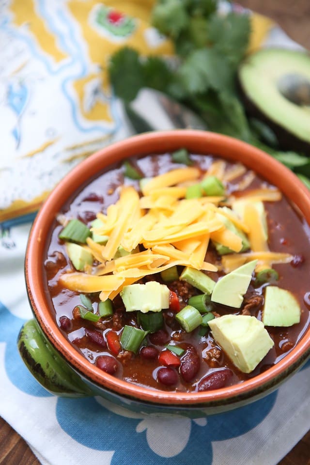 bowl of chili topped with shredded chicken, diced avocado, and scallions