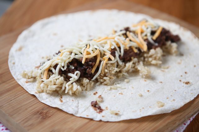 unwrapped tortilla being assembled with brown rice, ground turkey, and shredded cheese