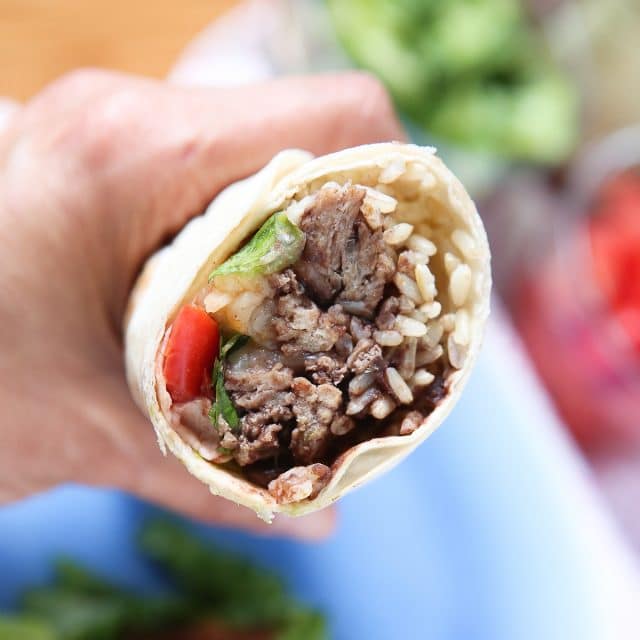 hand holding a wrapped turkey and black bean burrito with a bite, showing the fillings