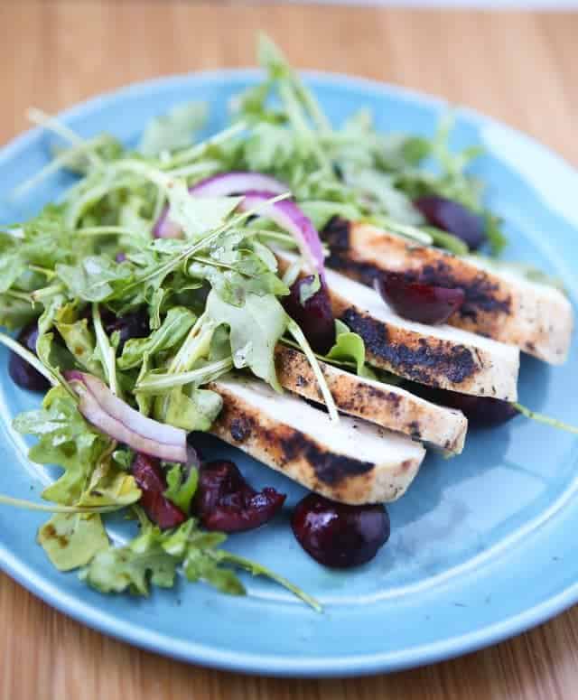 plate with grilled chicken, cherries, and red onions on a bed of arugula