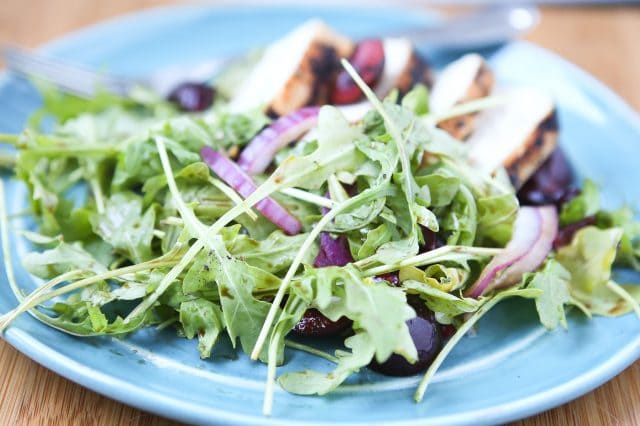 plate with grilled chicken, cherries, and red onions on a bed of arugula