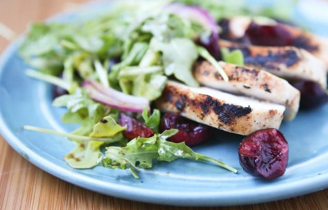 plate with grilled chicken, cherries, and red onions on a bed of arugula