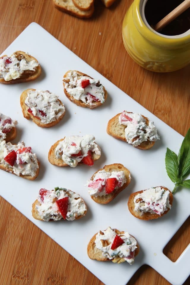 white platter with several snack toasts topped with goat cheese and strawberry spread