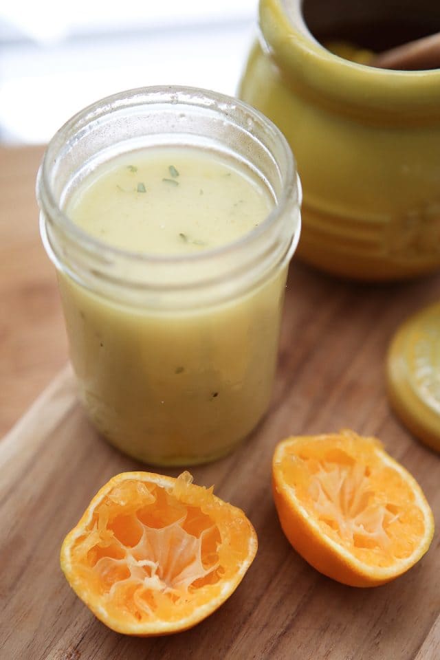 mason jar of clementine vinaigrette next to two halves of a clementine squeezed on a wooden cutting board