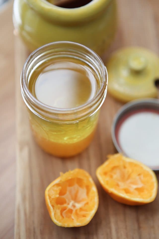 clementine vinaigrette being prepared in a mason jar alongside two halves of a squeezed tangerine on a wooden cutting board