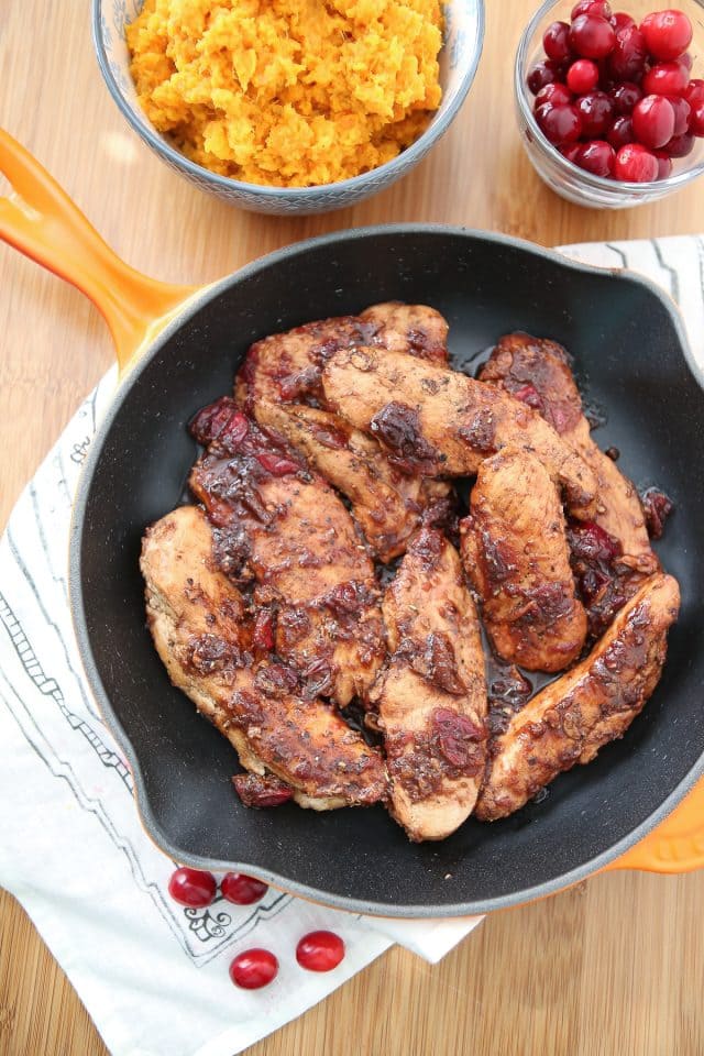 chicken in skillet covered in cranberry balsamic sauce next to container of cranberries