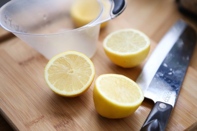 two lemons sliced in half on wooden cutting board with measuring cup and large knife