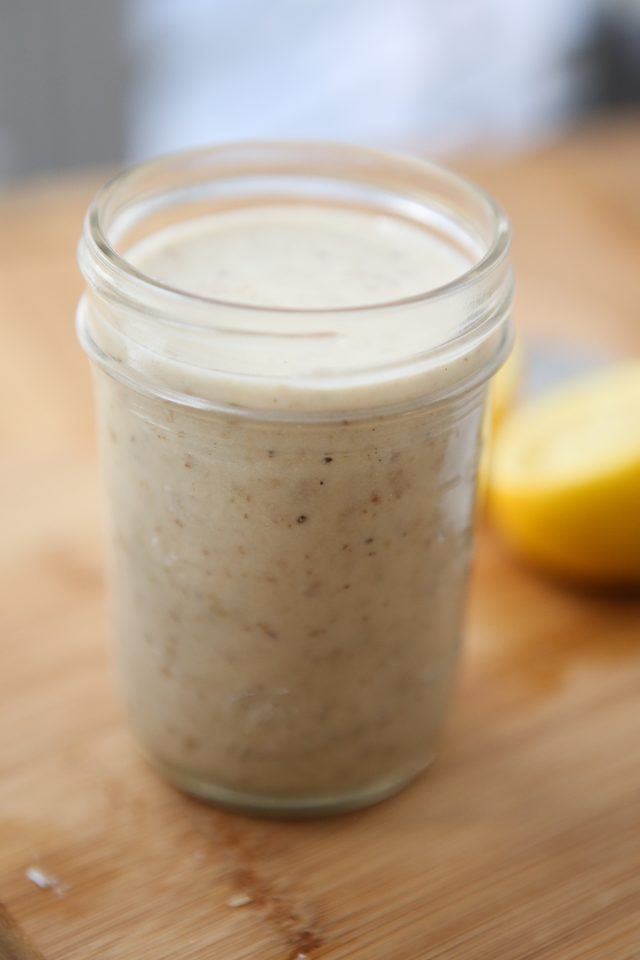 mason jar full of parmesan walnut lemon vinaigrette on a wooden cutting board with a lemon half in the background