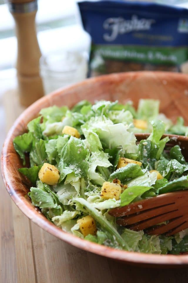 large wooden bowl of caesar salad topped with polenta croutons and parmesan walnut lemon vinaigrette