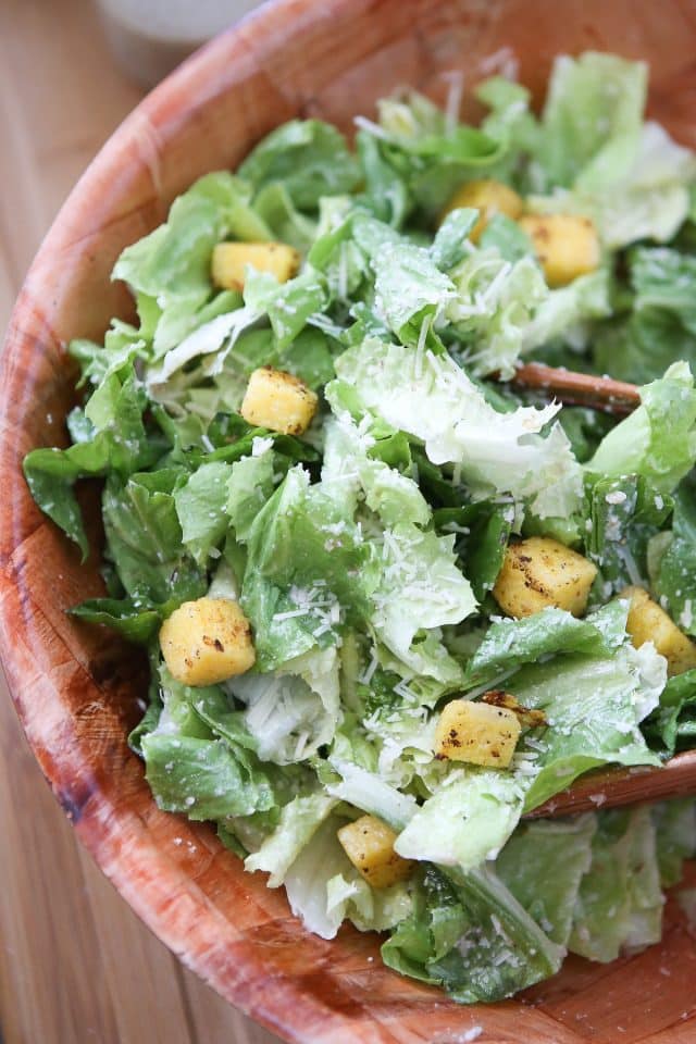 large wooden bowl of caesar salad topped with polenta croutons and parmesan walnut lemon vinaigrette