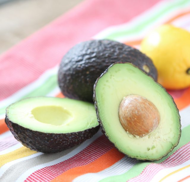 avocado sliced in half on a tablecloth next to a whole avocado and lemon