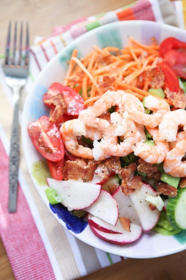 bowl of lettuce topped with cherry tomatoes, shrimp, radishes, cucumbers, carrots, and red peppers