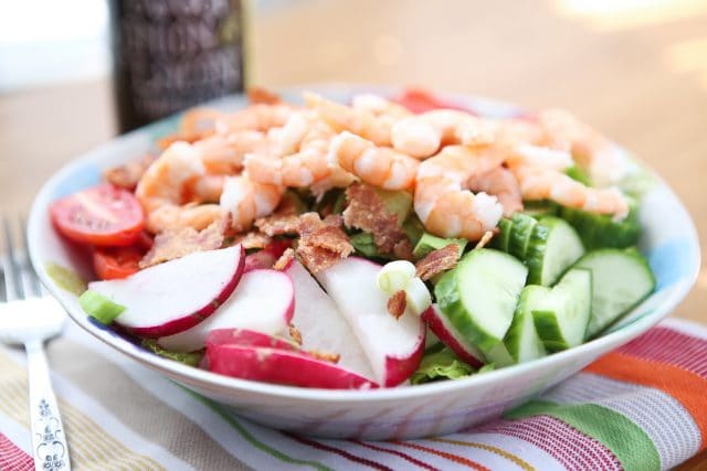 bowl of lettuce topped with cherry tomatoes, shrimp, radishes, cucumbers, carrots, and red peppers