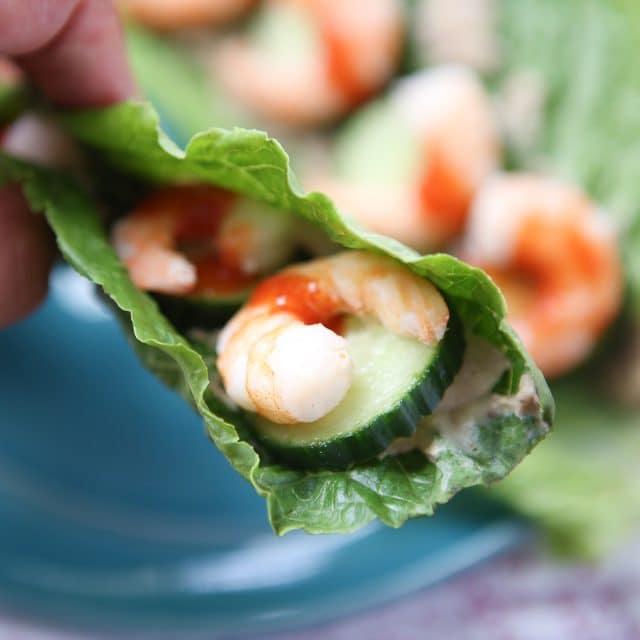 close up of romaine lettuce stuffed with shrimp and cucumber, drizzled with hot sauce