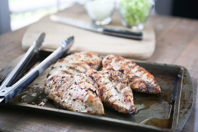 baking sheet of 4 pieces of grilled chicken with tongs to the side