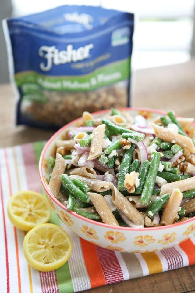 green bean pasta salad in a flowery bowl with bag of fisher nuts in the background