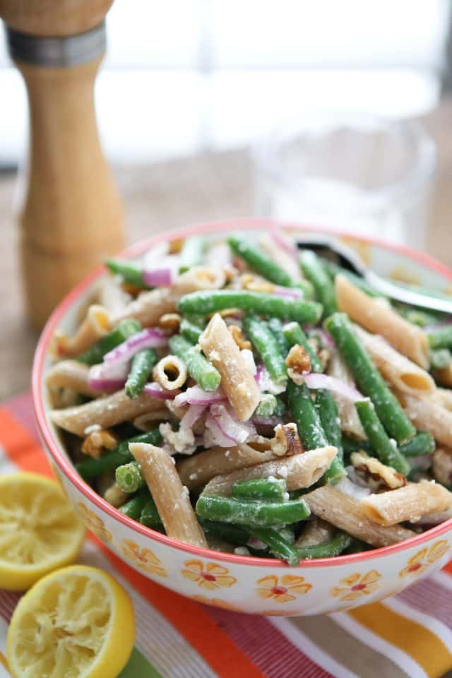 green bean pasta salad in a flowery bowl on a table with squeezed lemon, pepper mill and salt bowl in background