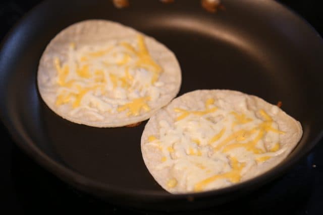 two tortillas with shredded melting cheese in a skillet