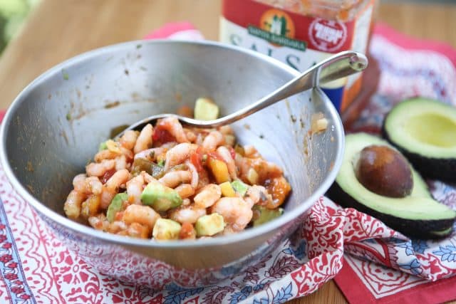 bowl with shrimp mix on a tapestry with an avocado cut in half and salsa