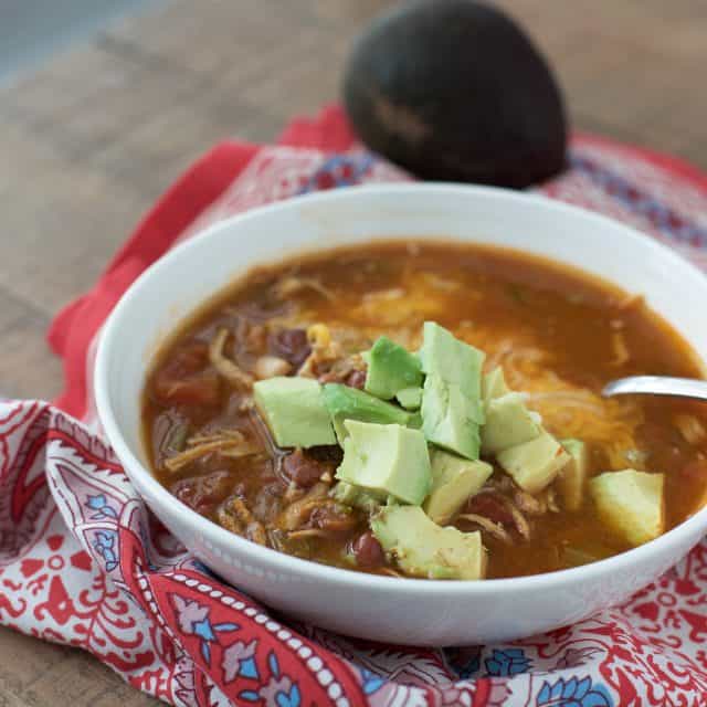 white bowl with chili flavored chicken soup topped with diced avocado