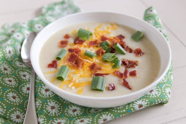 white bowl filled with cauliflower potato soup topped with cheese, green onion and bacon