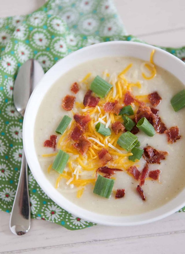 overhead shot of white bowl filled with cauliflower potato soup topped with cheese, green onion and bacon