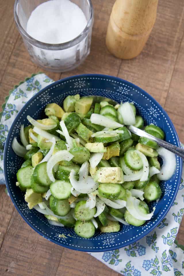 irisan mentimun, bawang bombay, dan alpukat potong dadu dalam mangkuk biru yang diberi lemon, garam, dan merica