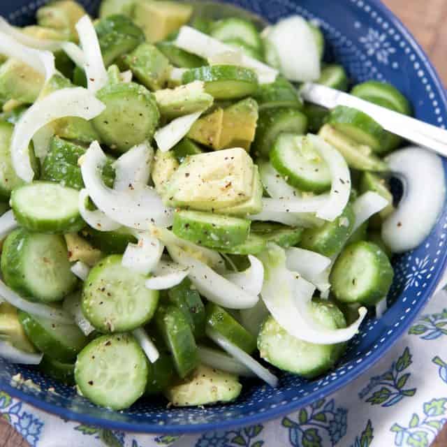 close up of cucumber, avocado and sliced onion salad in blue bowl